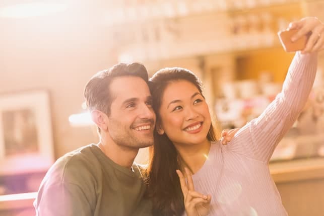 a mixed couple is smiling and taking selfies