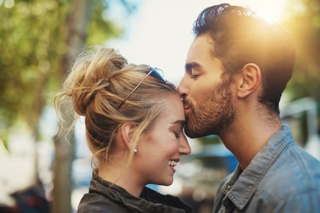 a man kisses his woman’s forehead outdoors