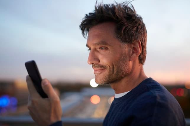 a mature man using his smartphone outdoors while smiling