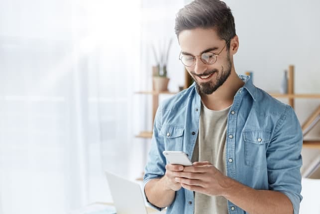 a handsome young man using his smartphone while smiling